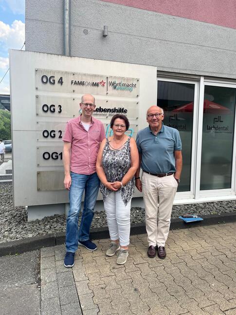 Sven Sieburg, Martina Merkert und Dr. Wolfgang Schröder (von links) stehen gemeinsam vor dem Gebäude der Lebenshilfe Lüdenscheid – Märkischer Kreis und symbolisieren die Übergabe der Ehrenamtskoordination. Das Foto dokumentiert den Wechsel und den Start des neuen Leitungsteams. Sven Sieburg, Martina Merkert und Dr. Wolfgang Schröder (von links) stehen gemeinsam vor dem Gebäude der Lebenshilfe Lüdenscheid – Märkischer Kreis und symbolisieren die Übergabe der Ehrenamtskoordination. Das Foto dokumentiert den Wechsel und den Start des neuen Leitungsteams.